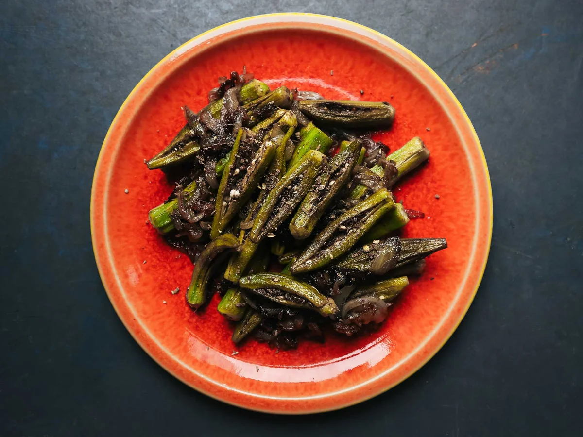 Sautéed okra pods with caramelized onions and herbs on a red plate.