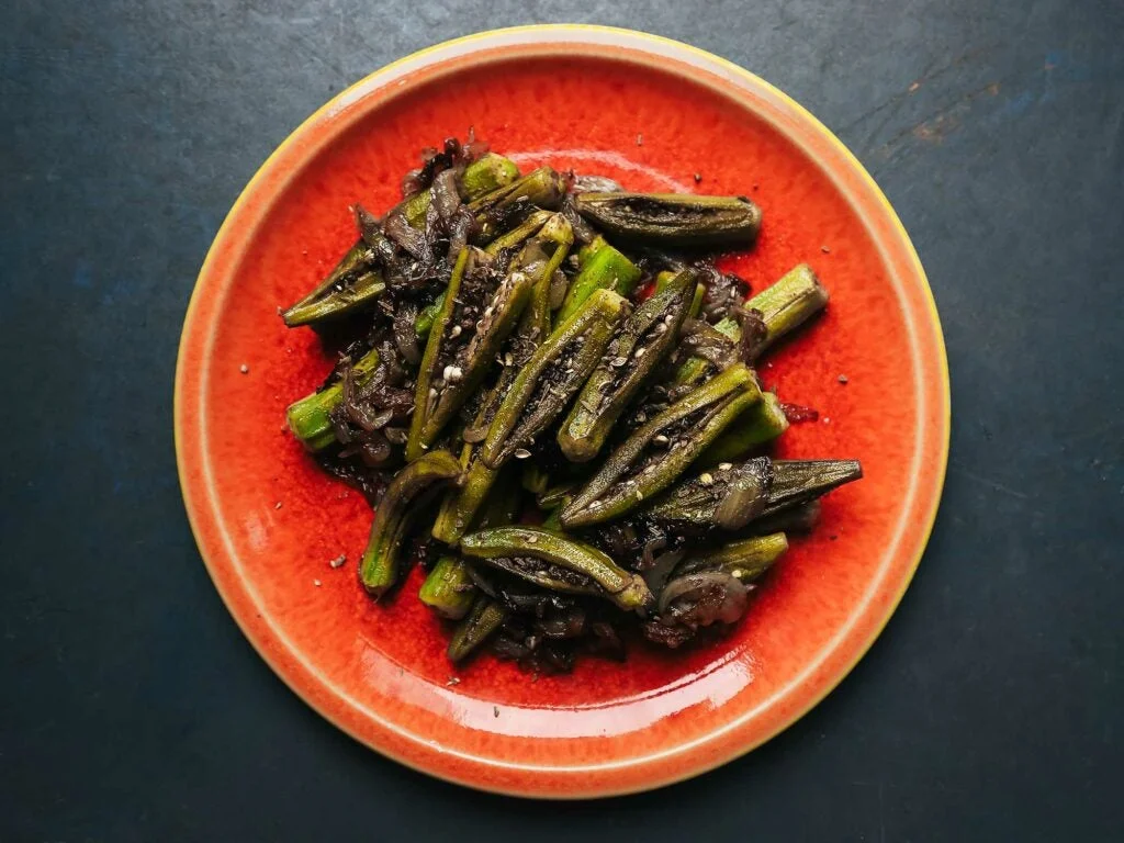 Sautéed okra pods with caramelized onions and herbs on a red plate.