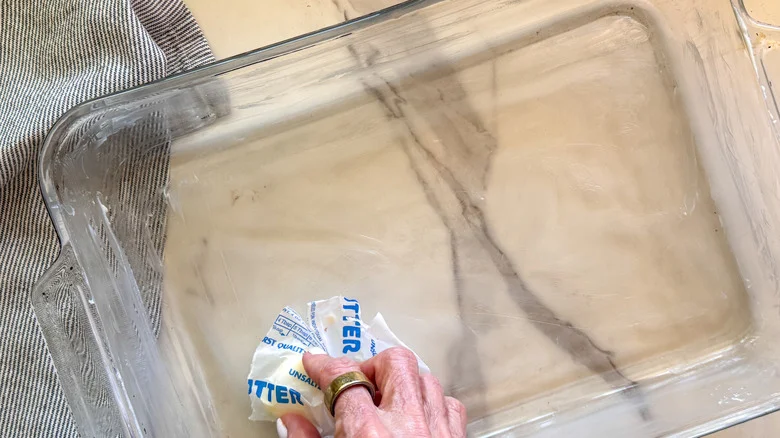 hand buttering the baking dish