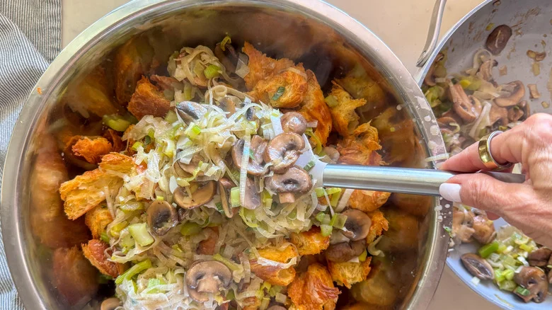 hand adding mushroom mixture to bowl