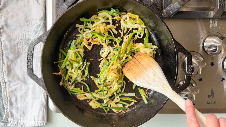 Sauteeing caramelized poblano pepper and sweet onion slices in cast iron skillet with wooden spoon