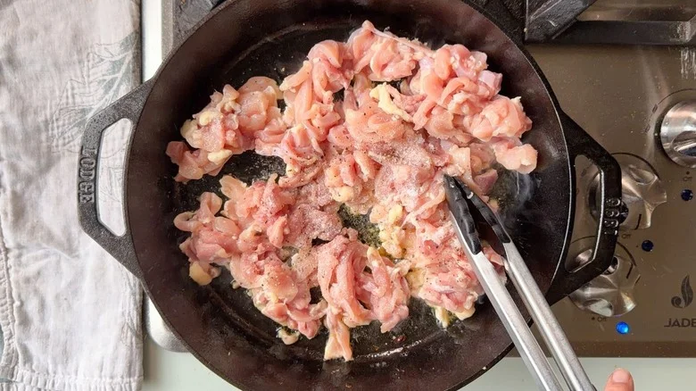 Thinly sliced raw chicken thighs in cast iron skillet on stovetop
