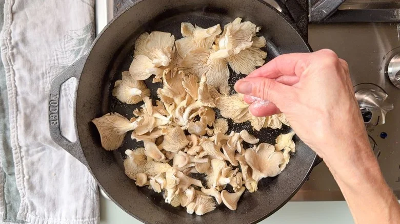 Salting oyster mushrooms in cast iron skillet on stovetop