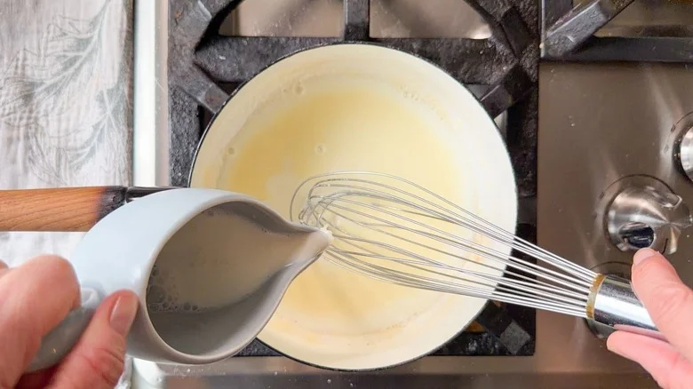 Pouring milk into roux in saucepan on stovetop