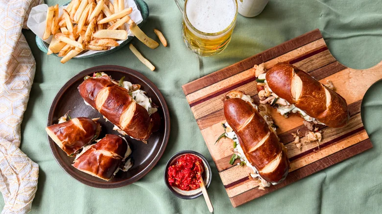 Chicken cheesesteak sandwiches on cutting board next to sandwiches on plate