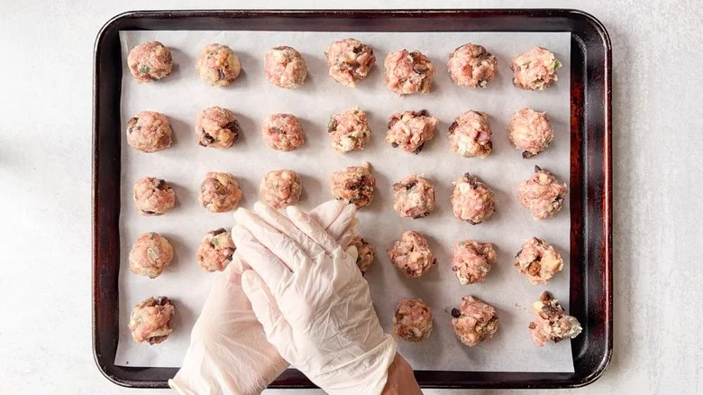Rolling meatballs by hand onto parchment-lined baking sheet wearing gloves