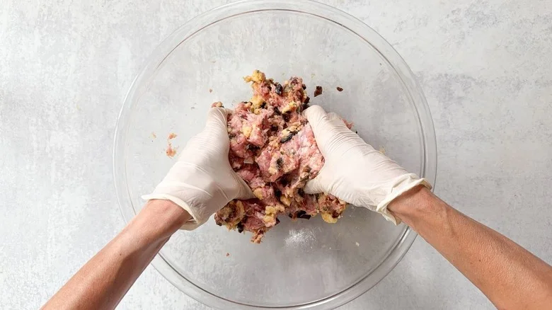 Mixing meatball ingredients together by hand wearing gloves in large glass bowl