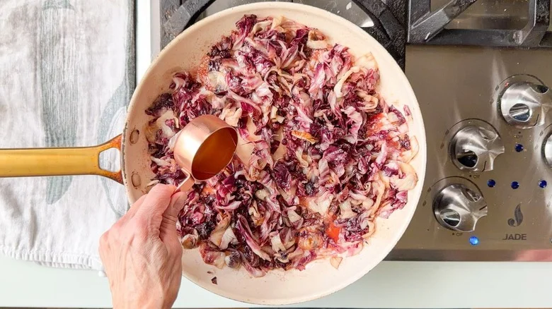 Adding chicken stock to charred radicchio in skillet on stovetop