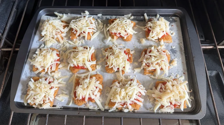 Chicken strips topped with marinara and mozzarella on baking sheet