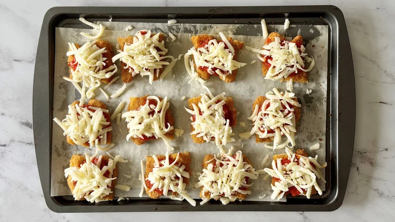 Portions of chicken strips topped with marinara and mozzarella on baking sheet