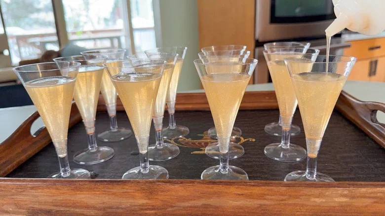 Pouring champagne jell-o shot mixture into mini champagne flutes on tray