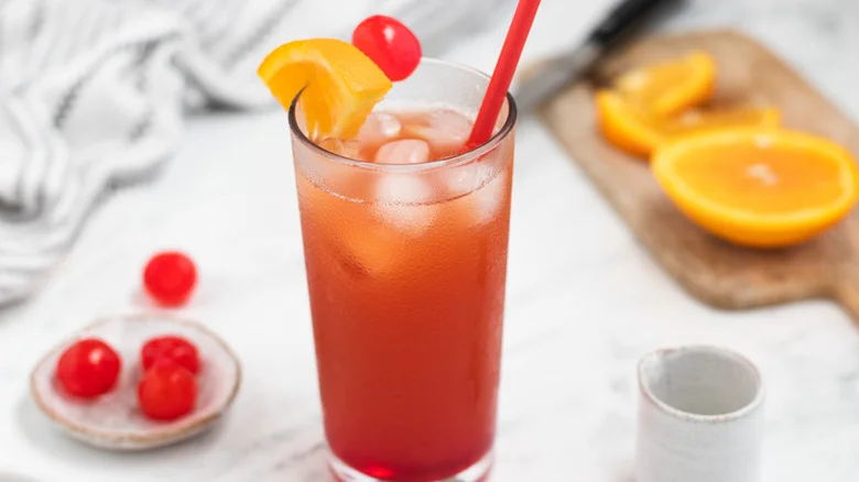 Orange Bahama mama cocktail in a highball glass, garnished with an orange wedge and a cherry