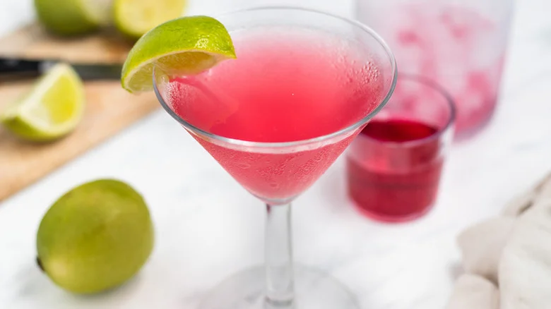 A bright pink cosmopolitan in a glass with a lime wedge