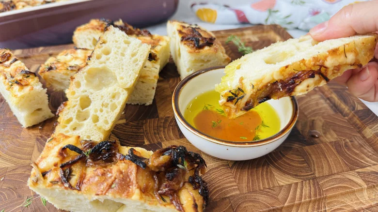 Hand dunking focaccia piece into olive oil next to more pieces of bread