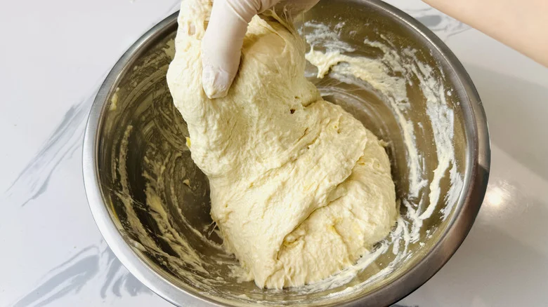Gloved hand stretching dough in bowl