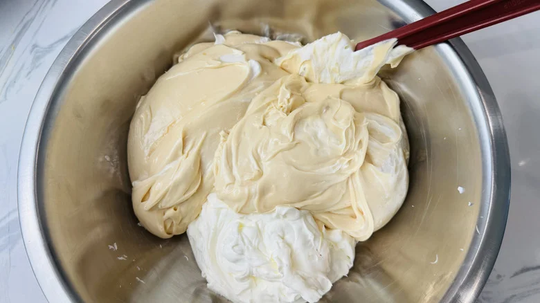 Caramel cream cheese mixture and whipped cream being mixed in bowl