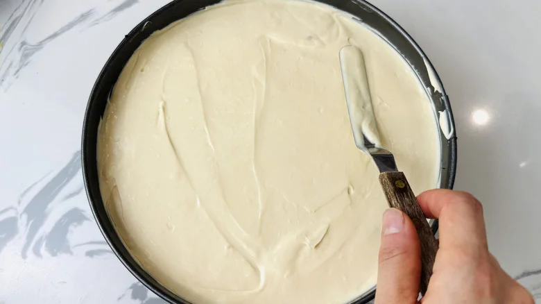 Hand smoothing out cheesecake filling in pan with offset spatula