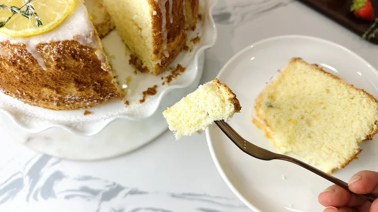 Fork holding bite of cake with whole cake and slice on plate in background