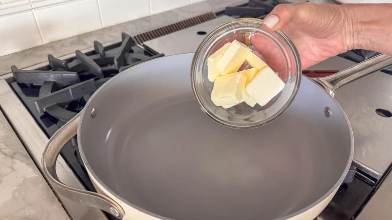 hand adding butter to pan