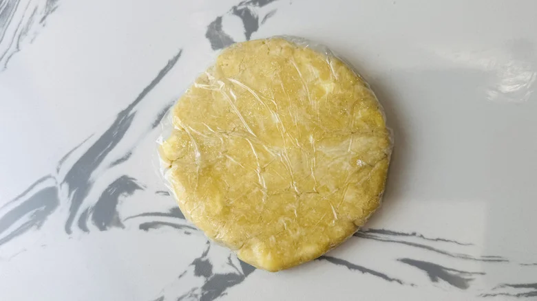 A disk of pie dough wrapped with plastic