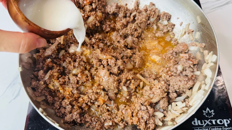 Hand pouring cornstarch slurry into beef mixture