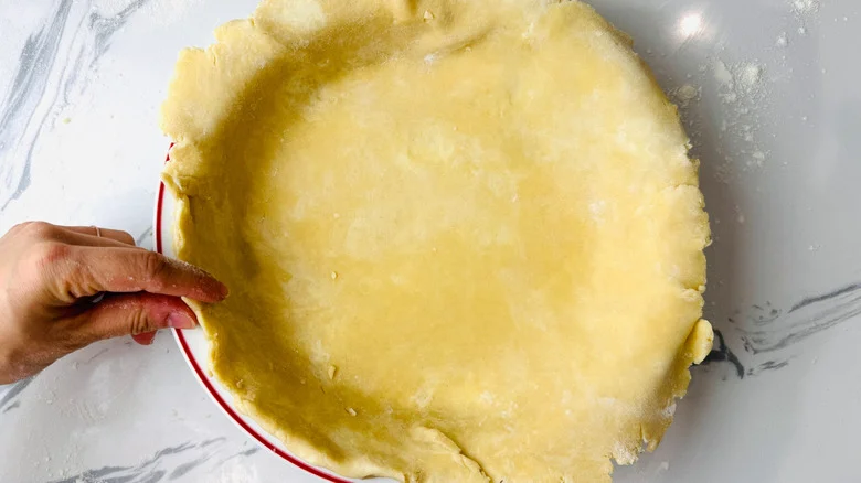 Hand pressing edge of pie crust in pie plate