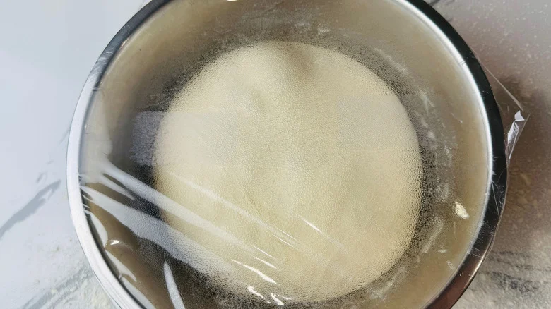 Dough in bowl covered with plastic wrap