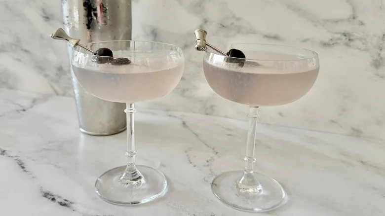 Aviation cocktails garnished with cherry skewers in front of cocktail shaker