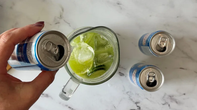 Hand pouring can of club soda into pitcher with limeade