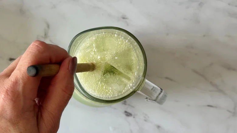 Hand using wooden spoon to stir limeade in pitcher