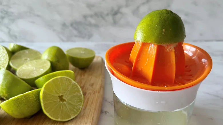 Lime half on juicer with more limes on wooden board