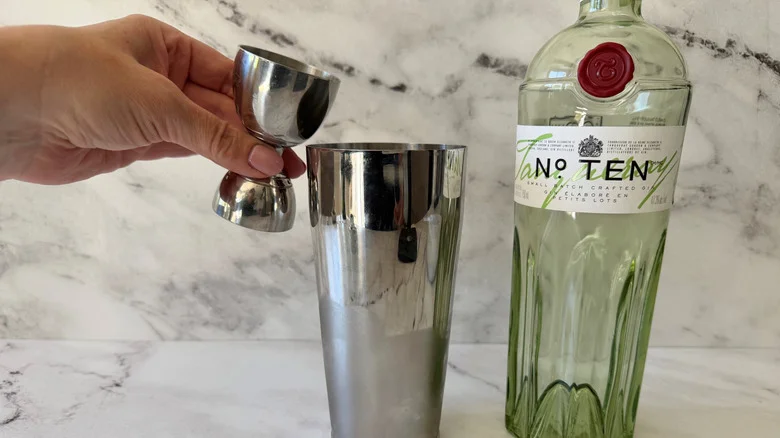 Hand pouring jigger with gin into cocktail shaker