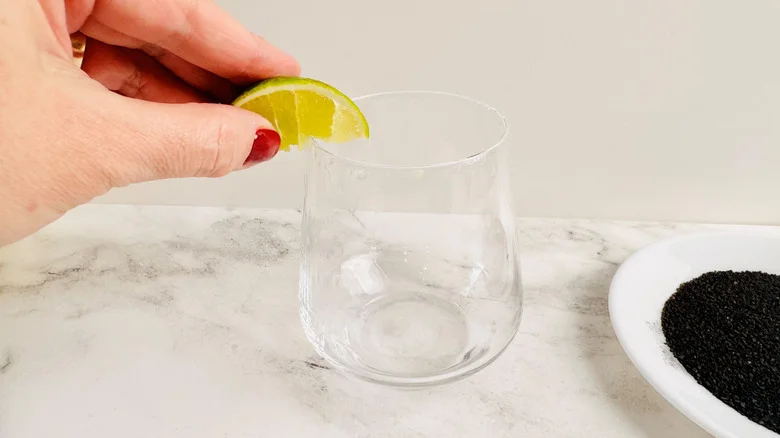 hand holding lime wedge over a drinking glass