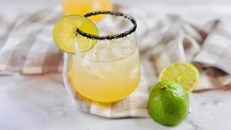 drink in a glass with a black salt rim and a lime garnish sitting on a crumpled checked cloth napkin