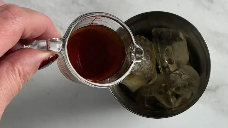 hand pouring syrup into a metal tumbler