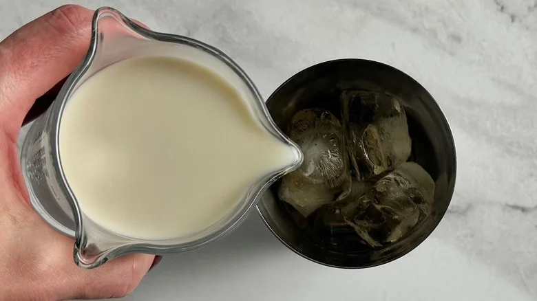 hand pouring milk into a metal tumbler