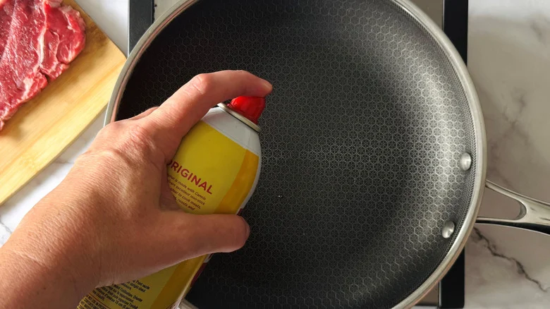hand spraying a frying pan with oil