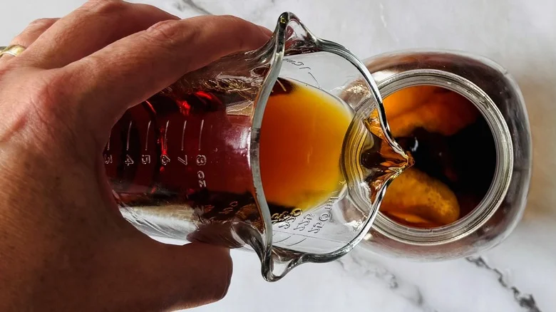 hand pouring brown liquid into a jar of fruit