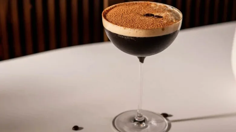 Foamy espresso martini in a tall round glass with cocoa powder on top.
