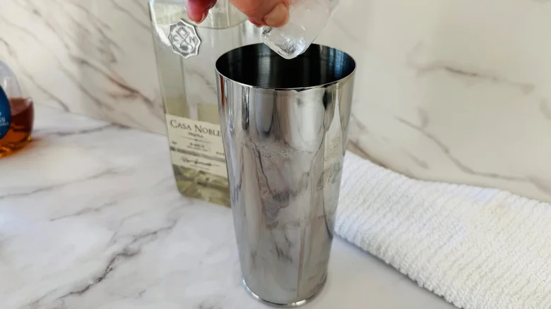 hand holding ice cubes over a cocktail shaker