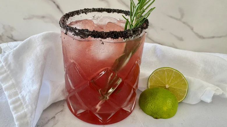 dark pink drink in a glass with ice and rosemary sticking out of the top