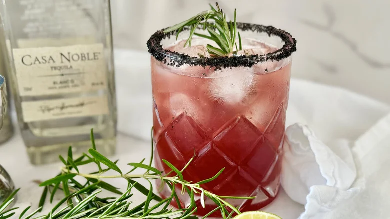 dark pink drink in a glass with ice and rosemary sticking out of the top