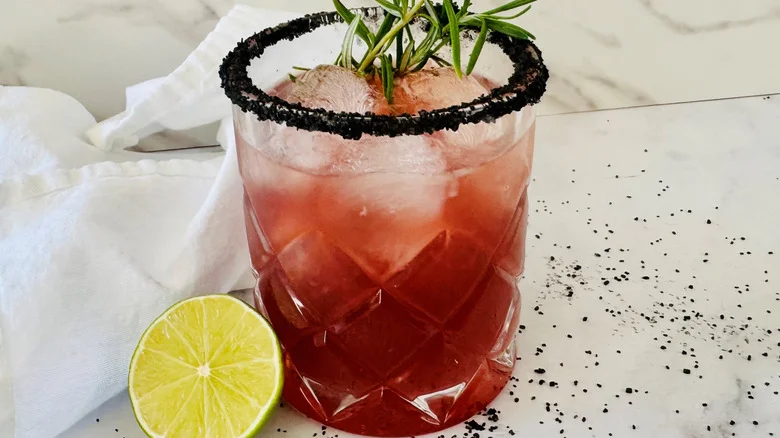dark pink drink in a glass with ice and rosemary sticking out of the top