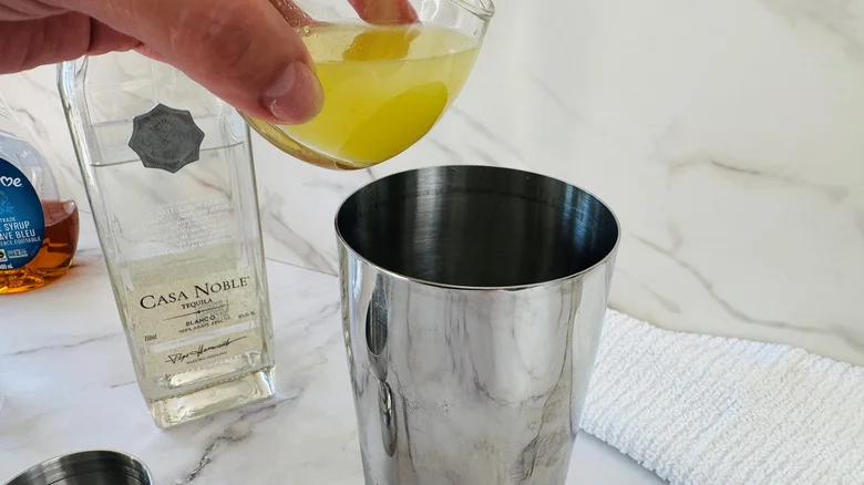 hand pouring lime juice into a cocktail shaker