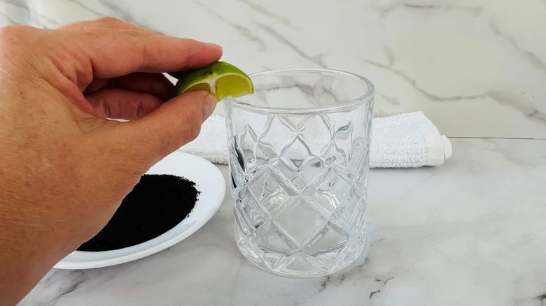 hand holding a piece of lime over a drinking glass