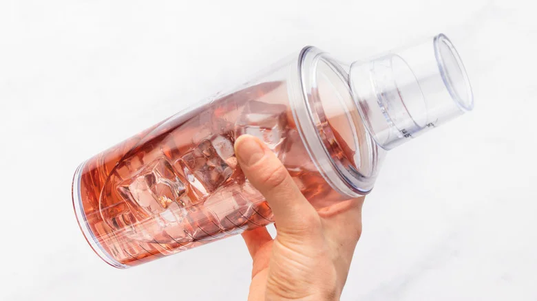 Shaking pink cocktail and ice in shaker