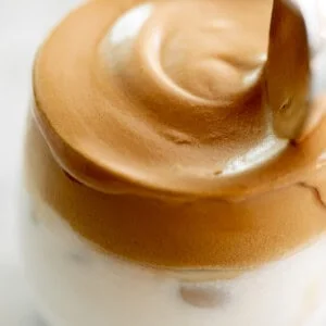 Whipped dalgona coffee on top of a glass full of milk.
